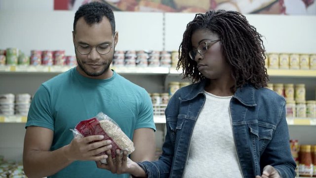 Focused people buying groats in store. Serious young couple shopping together. Shopping concept