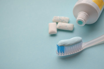 A white toothbrush with blue toothpaste, tube of toothpaste, mint gum pads on a light blue background. Concept of alternative oral hygiene, fresh breath. Copy space