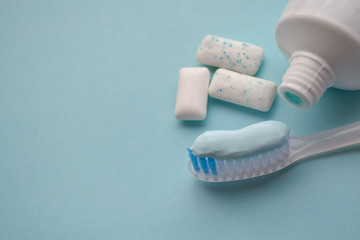 A white toothbrush with blue toothpaste, tube of toothpaste, mint gum pads on a light blue background. Concept of alternative oral hygiene, fresh breath. Copy space