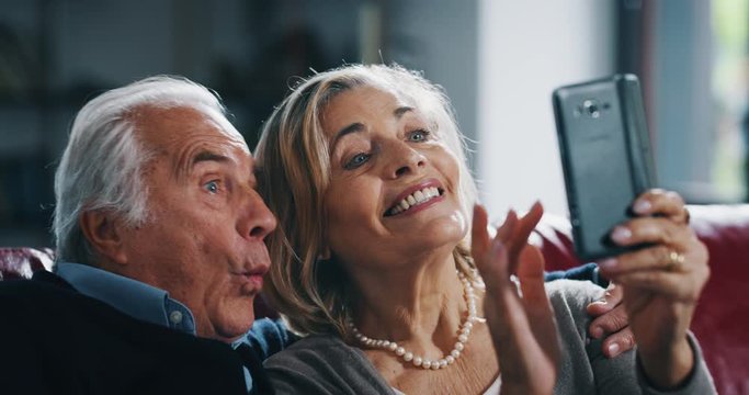 Close up of happy mature senior couple is taking selfie with a smartphone in living room.