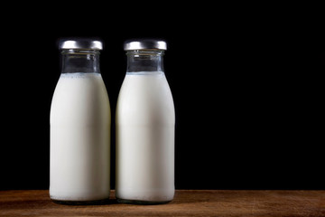 Two glass bottles of fresh milk on a black background.