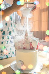 Cake decoration female hands in a frame in a bright kitchen sprinkles gingerbread houses powdered sugar snow Christmas treat for the holiday magic lights garlands