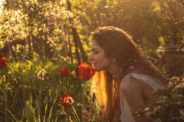Girl in white dress smelling tulip in sunset among fluff, dandelions and cherry flowers