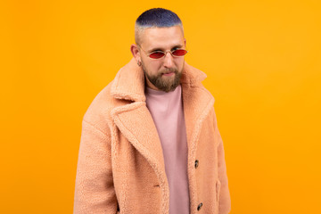Brutal caucasian man with short blue hair and red glasses in a fur coat gesticulates isolated on...