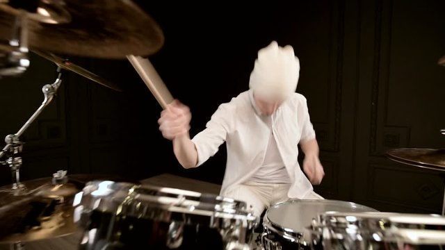 Handsome guy in white actively plays on drum kit in on black background. Closeup
