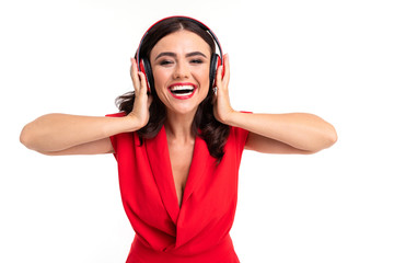 glamorous girl in a red dress enjoys listening to music on headphones on a white wall