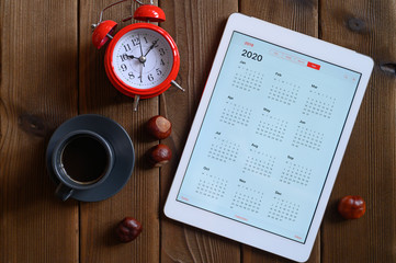a tablet with an open calendar for 2020, a Cup of coffee, chestnuts and a red alarm clock on a...