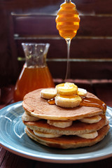 A stack of banana pancakes on a blue plate. Pancakes pour honey or maple syrup.Traditional American Breakfast. The concept of home made healthy food. Vertical.