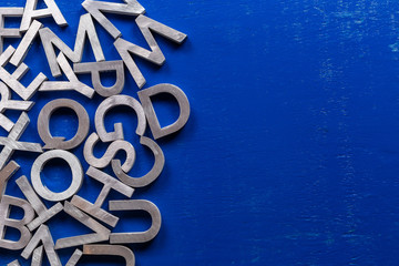 Flat mockup of silver metal alphabet characters on blue painted board background with copyspace. © lucky pics