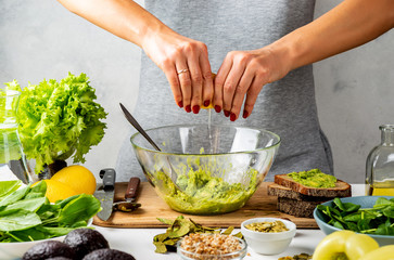 Woman squeezes juice from a lemon in a glass bowl with avocado guacamole. healthy food concept.