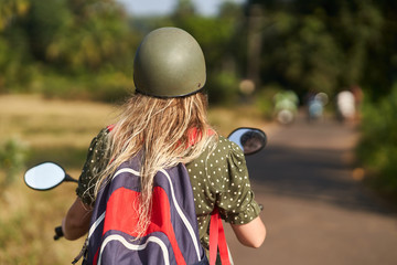Fototapeta na wymiar A girl in a green dress drives a scooter. 