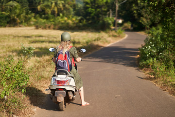 A girl in a green dress drives a scooter. 