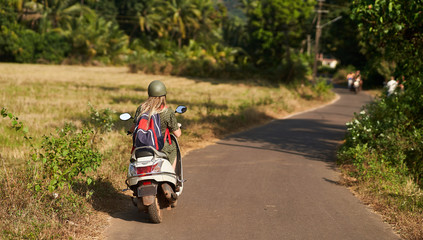 A girl in a green dress drives a scooter. 