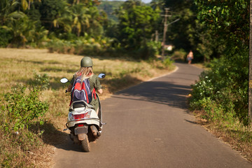 A girl in a green dress drives a scooter. 
