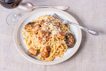 Spaghetti with homemade sausages and eggplant sprinkled with grated cheese in a plate and a glass of red wine on the table - a traditional Italian rural lunch