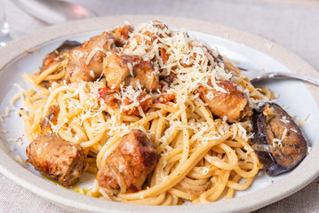 Spaghetti with homemade sausages and eggplant sprinkled with grated cheese in a plate close-up, top view - traditional Italian pasta