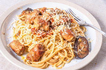 Spaghetti with homemade sausages and eggplant sprinkled with grated cheese in a plate close-up, top view - traditional Italian pasta