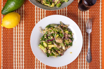 Healthy tuna, avocado and cucumber salad with onions in a plate on a table with ingredients - american cuisine
