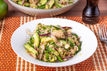 Healthy tuna, avocado and cucumber salad with onions in a plate on a table with ingredients - american home cooking