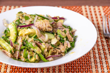 Healthy tuna, avocado and cucumber salad with onions in a plate on a table close-up - american home cooking