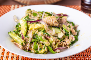 Healthy tuna, avocado and cucumber salad with onions in a plate on a table close-up - american home cooking