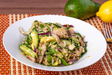 Healthy tuna, avocado and cucumber salad with onions in a plate on a table with ingredients - american cuisine