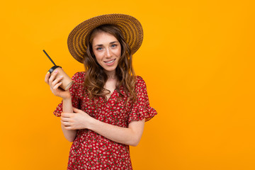 studio portrait of a charming stylish smiling girl in a hat and a red dress with a paper cup on an orange background