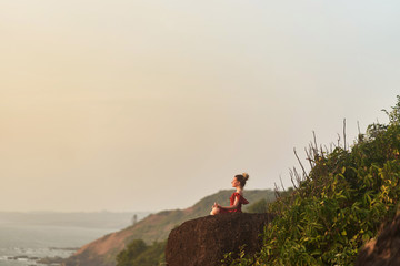 Fototapeta premium Young girl practices yoga in a red dress on a mountain in India
