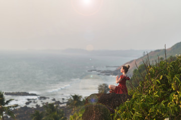 Young girl practices yoga in a red dress on a mountain in India