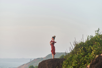 Young girl practices yoga in a red dress on a mountain in India