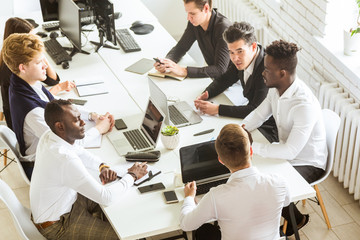 A team of young businessmen sitting at the table, top view, working and communicating together in an office. Corporate businessteam and manager in a meeting.