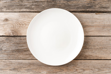 Empty white dish on rustic wooden table. Top view