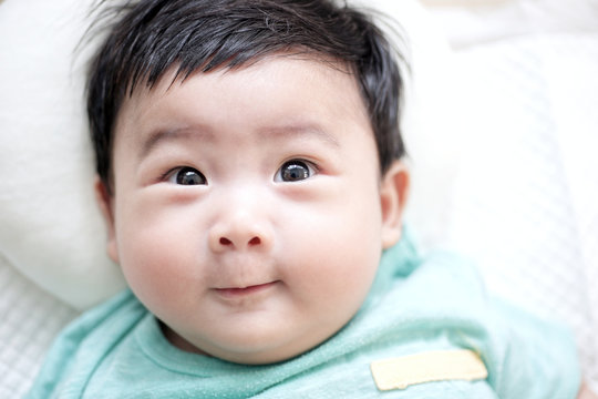 Cute adorable asian newborn looking at camera and smiling on white bed : Closeup