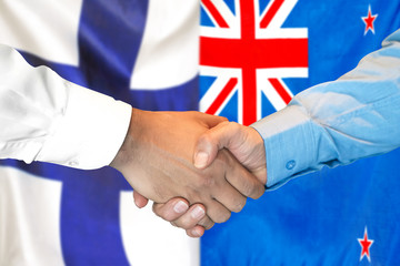 Handshake on Finland and New Zealand flag background.