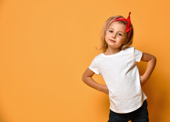 Beautiful little girl in a white T-shirt and a red bandage on her head with blue eyes looks slyly...