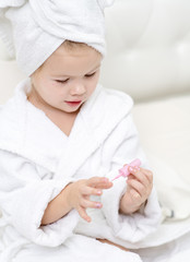 Obraz na płótnie Canvas little cute girl painting her nails on the bed in the bedroom in a towel and Bathrobe