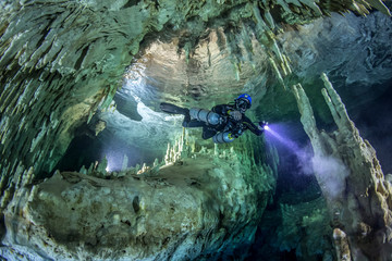 A cave diver swims in the Hulo cenote (Mexico), illuminated by the AMG's underwater light. Karst cave, formed stalactites and stalagmites are visible. © Дмитрий Ефремычев