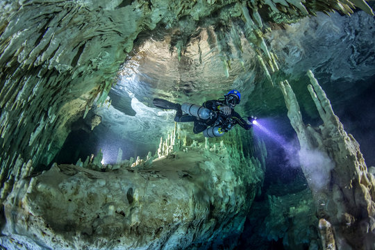 A cave diver swims in the Hulo cenote (Mexico), illuminated by the AMG's underwater light. Karst cave, formed stalactites and stalagmites are visible.