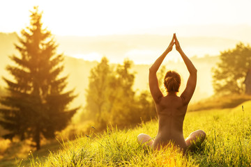 Nude woman practices yoga in nature