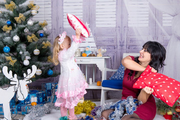 Happy and funny mom and daughter are playing pillow fights for Christmas.