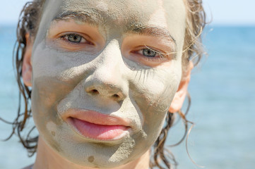 close up portrait of a young woman with a mask on her face made of blue healing clay, outdoors at sea