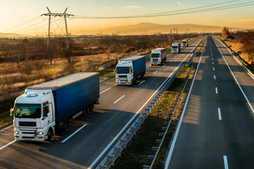 High speed Lorry trucks in line as a caravan or convoy on a country highway under a beautiful sunset sky