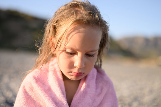 sad six year old little girl resting on the sea beach after swimming