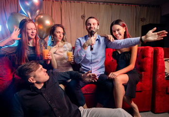 young caucasian friends have fun together at karaoke bar, wearing dress and t-shirt, trendy modern clothes. indoors of karaoke room with neon lights - obrazy, fototapety, plakaty