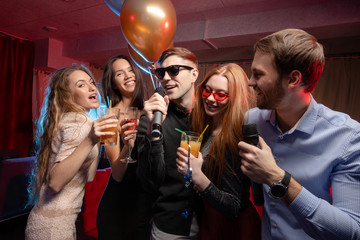 Photo of pretty girls and handsome guys singing in mic at party with friends, indoors of karaoke....
