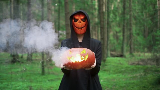 Female in coak takes pumpkin with smoke on the halloween in autumn forest