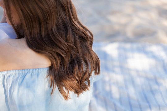 Woman's back. Brown curls on the back. Curly girl sitting on the sand on striped rug