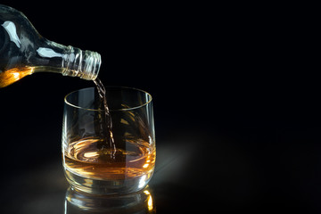 Pouring whiskey into glass. Free space for text, dark background.