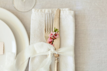 Table setting for a dinner with flowering cherry tree branches on the table. Vintage knife and fork on the white linen tablecloth