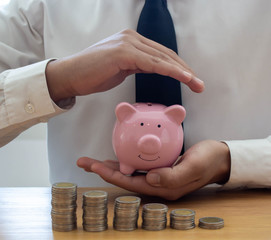 A businessman holding a piggy bank with coins on the wooden table